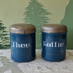 Op de afbeelding: Twee vintage blauwe metalen kannen met zilveren deksels. De kannen zijn gelabeld "Thee" en "Koffie".