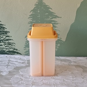 May include: A clear plastic container with a yellow lid. The container has two compartments and is designed for storing food.