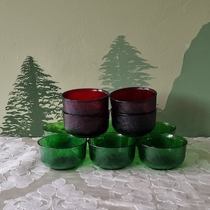 May include: A set of eight glass bowls, stacked in a pyramid shape. The bowls are green and red, with a textured surface. The bowls are on a white tablecloth.