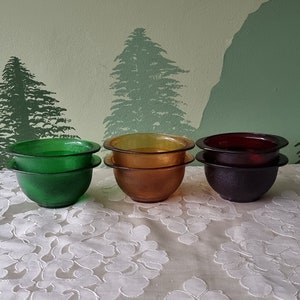Op de afbeelding: Vier glazen kommen in verschillende kleuren: groen, geel, oranje en rood. De kommen zijn op elkaar gestapeld.