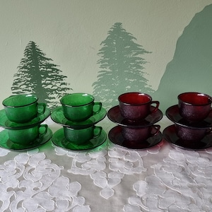 Op de afbeelding: Zes vintage theekopjes en schoteltjes, drie groen en drie rood, gerangschikt op een wit kantkleed.