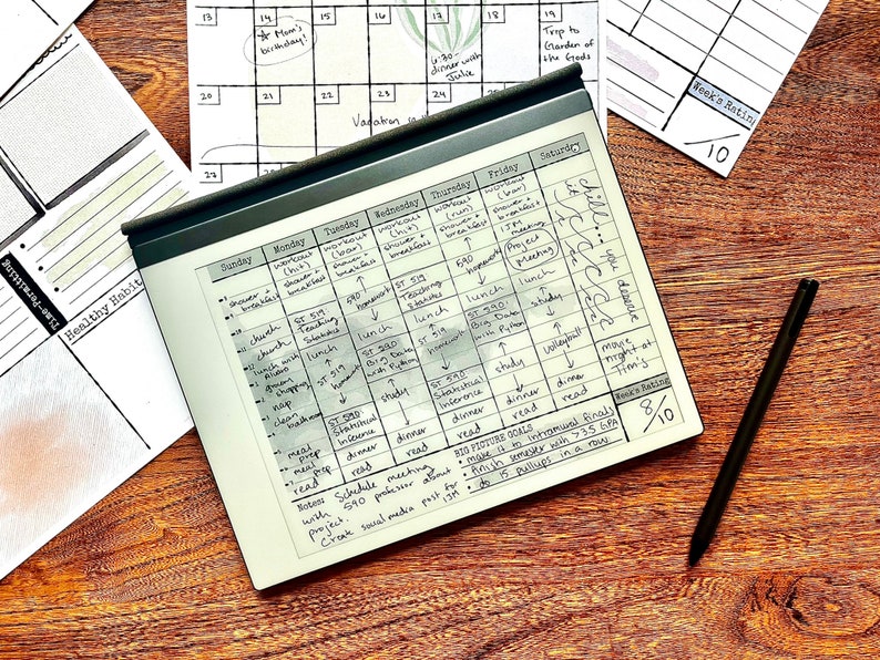 May include: A black and white weekly planner with handwritten notes and a schedule for the week. The planner is on a wooden surface with a black stylus next to it. The planner has a book rating section with a score of 8 out of 10.