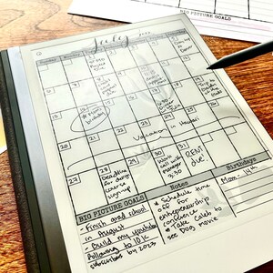 May include: A white digital calendar with a black frame and a black stylus. The calendar is open to July and has handwritten notes and appointments. The notes include "Mom's birthday", "Vacation in Hawaii", "Rent due", and "Schedule time off for entrepreneurship conference".
