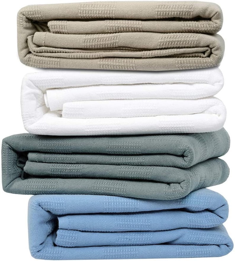 May include: A stack of four folded blankets in different colors: beige, white, gray, and blue. The blankets are made of a soft, textured fabric.