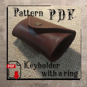 Peut inclure: Un porte-clés en cuir marron avec un anneau et une fermeture à bouton. Le texte "Pattern PDF" et "Keyholder with a ring" est visible sur l'image.