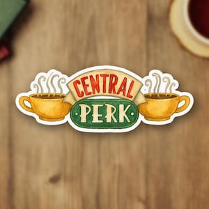 以下が含まれることがあります： テレビ番組「フレンズ」の「セントラルパーク」ロゴのステッカー。デザインには、湯気の立つ2つの黄色のコーヒーカップと、「セントラルパーク」という言葉が赤と緑で書かれたバナーが含まれています。