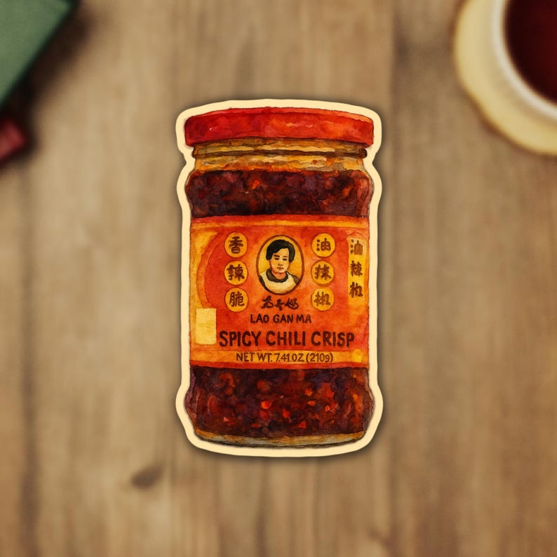 Peut inclure: Autocollant repr&eacute;sentant un pot de Lao Gan Ma Spicy Chili Crisp. Le pot a un couvercle rouge et une &eacute;tiquette avec des caract&egrave;res chinois et le texte "SPICY CHILI CRISP". Le poids net est de 210 grammes.