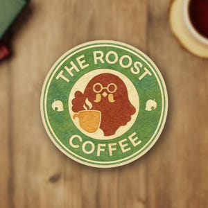 Op de afbeelding: Een ronde sticker met een groene en beige rand met de tekst "THE ROOST COFFEE". Het midden toont een bruin, uilachtig personage met een bril die een gele koffiekop vasthoudt. Kleine bladiconen aan de zijkanten.