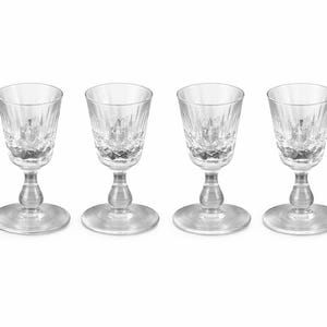 May include: Four clear crystal shot glasses with a cut-glass design. Each glass has a round base, a stem, and a flared rim. The glasses are arranged in a row against a white background. Ideal for serving spirits.