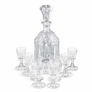 May include: A clear crystal drinks decanter with a stopper, accompanied by eight matching shot glasses. The decanter and glasses have a cut glass pattern. The set is displayed against a white backdrop.