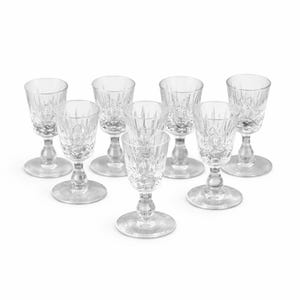 May include: A set of eight clear crystal cordial glasses. Each glass has a round base, a slender stem, and a detailed, patterned bowl. The glasses are arranged on a white background, highlighting their elegant design.