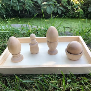 May include: A wooden tray with four wooden toys: a ball in a bowl, a doll with a round head, and two eggs in egg cups.