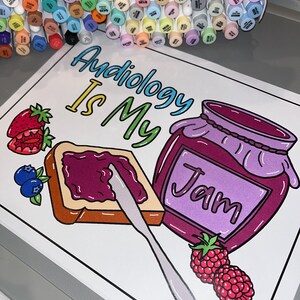 以下が含まれることがあります： ジャムの入った瓶、ジャムを塗ったパン、ナイフ、ラズベリーが描かれた白い塗り絵。 「Audiology is my jam」という文字がカラフルな文字で書かれている。ページには「SLP Krit」という署名がある。