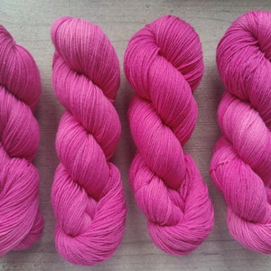 Op de afbeelding: Vier bollen roze garen, elke bol is gedraaid in de vorm van een acht.