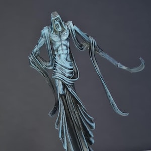 Op de afbeelding: Een blauwgrijze miniatuurfiguur van een spookachtige krijger met vloeiende gewaden en uitgestrekte armen. De figuur staat op een getextureerde basis met schedels en groene accenten. De figuur is beschilderd met gedetailleerde schaduwen.