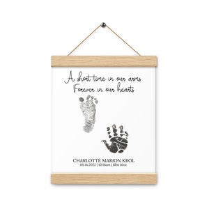 Könnte beinhalten: Ein weißer gerahmter Druck mit schwarzen Tinten-Hand- und Fußabdrücken. Der Text lautet "A short time in our arms Forever in our hearts" und "CHARLOTTE MARION KROL 06.14.2022 | 10:16am | 8lbs 10oz".
