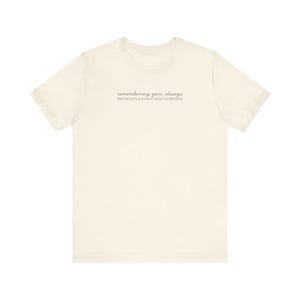 May include: Cream-colored t-shirt with the text "remembering you, always" and "PREGNANCY & INFANT LOSS AWARENESS" printed in a delicate, light gray font. The shirt has short sleeves and a crew neck.