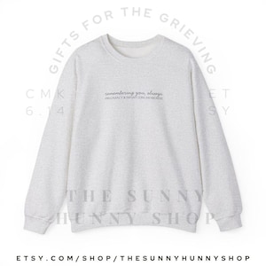 May include: A light gray sweatshirt with the text "remembering you, always" and "PREGNANCY & INFANT LOSS AWARENESS" in a delicate font. The sweatshirt also has the text "GIFTS FOR THE GRIEVING" and "THE SUNNY HUNNY SHOP". The Etsy shop URL is visible.