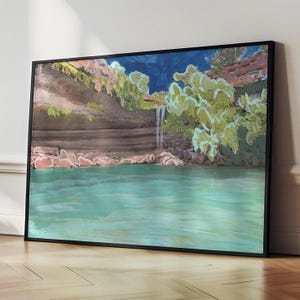 May include: A framed landscape painting depicting a waterfall cascading into a turquoise pool. The artwork features a dark blue sky, green foliage, and brown rock formations. The painting is in a black frame and rests on a wooden floor.