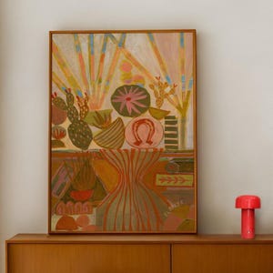 Puede incluir: Pintura abstracta en un marco de madera con cactus, una herradura y un diseño floral en tonos rosa, verde y naranja. La pintura se exhibe sobre un mueble de madera, con una lámpara roja a la derecha.