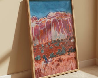 May include: A framed vertical art print featuring a painted landscape with tall red rock formations under a blue sky. In the foreground, a figure rides a white horse through a field of reddish-brown grasses and small green shrubs, all encased in a light wood frame.