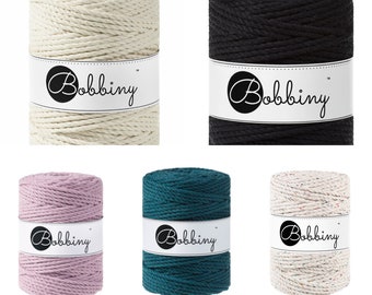 Puede incluir: Seis carretes de cuerda de algodón en varios colores, incluyendo natural, negro, rosa polvoriento, azul pavo real y polvo de arcoíris. Cada carrete tiene una etiqueta blanca con la palabra "Bobbiny" en un círculo negro.