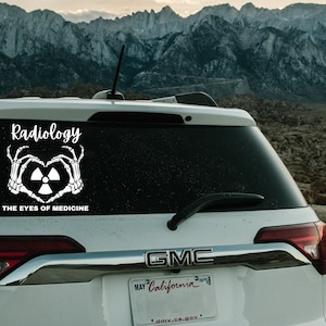 May include: White car with a black window sticker that says "Radiology The Eyes of Medicine" with a white skeleton hand making a heart shape around a white radiation symbol. The car has a GMC logo and a California license plate.