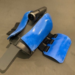 May include: A blue and black wrist brace with a strap and a small black attachment on top.