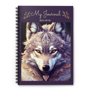 Könnte beinhalten: Lilafarbenes Spiralnotizbuch mit den Worten "My Journal Believe" auf dem Cover. Das Cover zeigt eine detaillierte Illustration eines Wolfskopfes mit einer Blumenkrone.