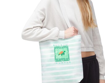 May include: A white tote bag with a light green and white striped pattern. The bag features a square design with a sea turtle illustration in shades of green and orange. The bag has a white strap.
