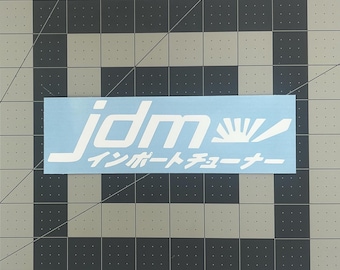 May include: White vinyl sticker with the text "jdm" in a stylized font and the Japanese text "インポーターチューナー" below. The sticker is on a light blue background.