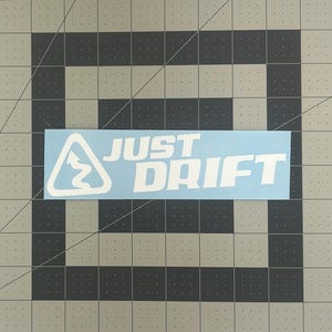 May include: White vinyl decal with a winding road symbol and the text "JUST DRIFT" on a light blue background.