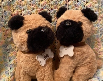 May include: Two plush brown and black pug dog toys with a bone-shaped tag that says "I love dog" on one of the dogs. The dogs are sitting on a multi-colored crocheted blanket.