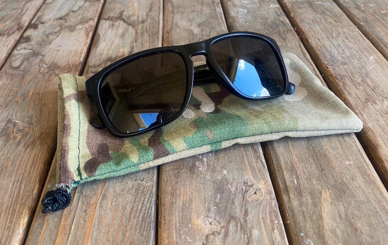 May include: Black sunglasses with a camouflage fabric case. The sunglasses have a rectangular frame and dark lenses.