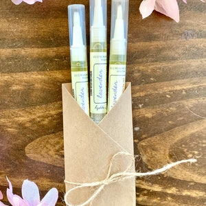 May include: Three small bottles of lavender essential oil packaged in a brown paper envelope tied with twine. The bottles are labeled "lavender essential oil" and have a white cap with a brush applicator.
