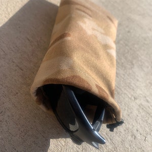 K&ouml;nnte beinhalten: Eine Stofftasche mit Tarnmuster und Rei&szlig;verschluss, die eine schwarze Sonnenbrille enth&auml;lt.