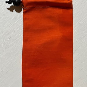 K&ouml;nnte beinhalten: Orangefarbene Kordeltasche mit schwarzem Kordel und Stopper.