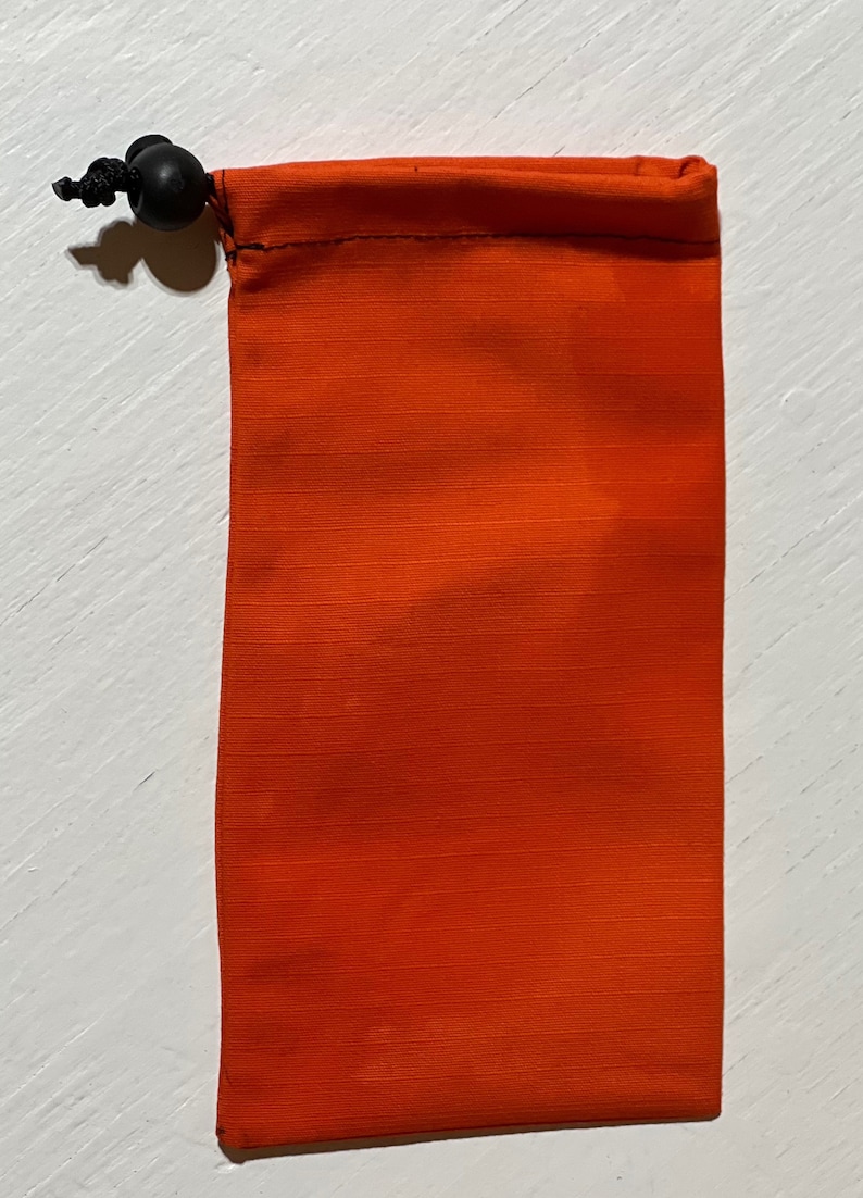 K&ouml;nnte beinhalten: Orangefarbene Kordeltasche mit schwarzem Kordel und Stopper.