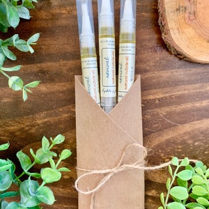 May include: Three clear plastic tubes with a brown paper wrapper tied with twine. Each tube contains a clear liquid and has a white applicator tip. The label on the tubes reads "revival natural cuticle oil".