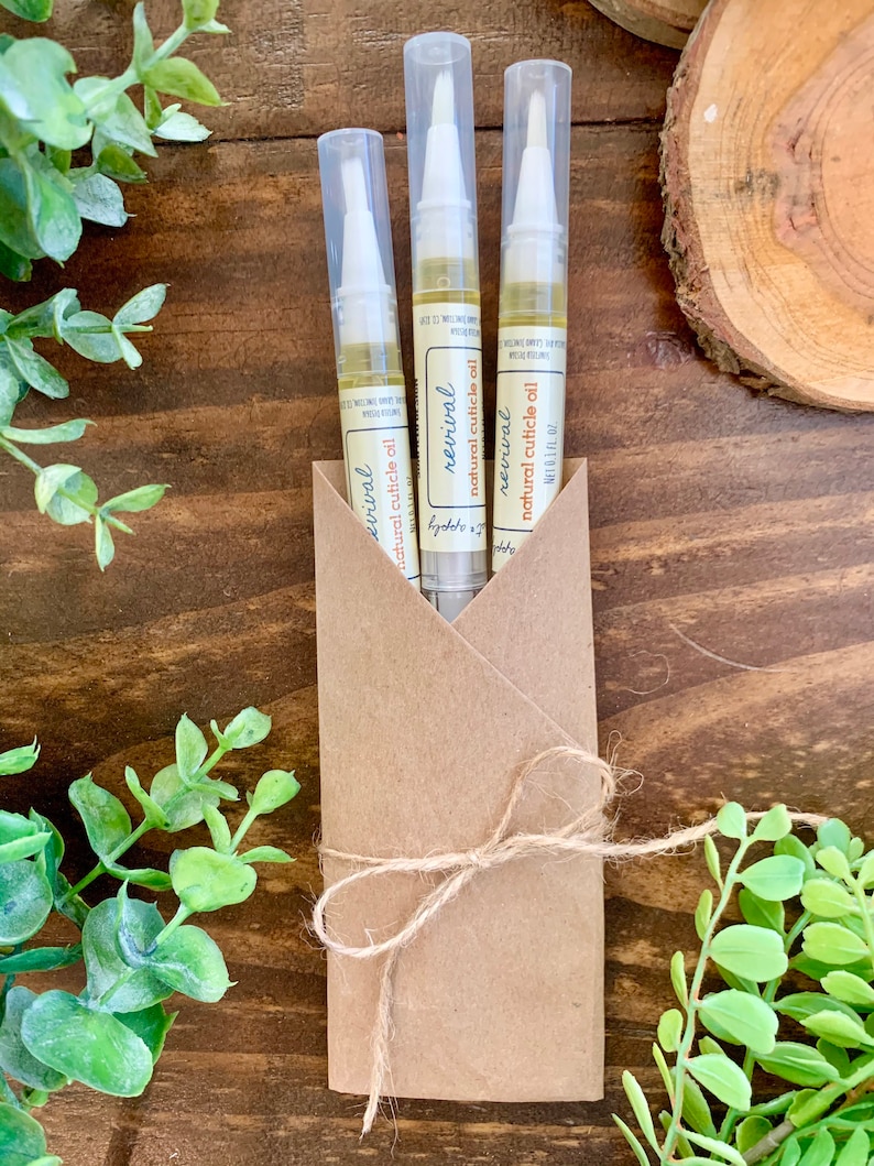 May include: Three clear plastic tubes with a brown paper wrapper tied with twine. Each tube contains a clear liquid and has a white applicator tip. The label on the tubes reads "revival natural cuticle oil".