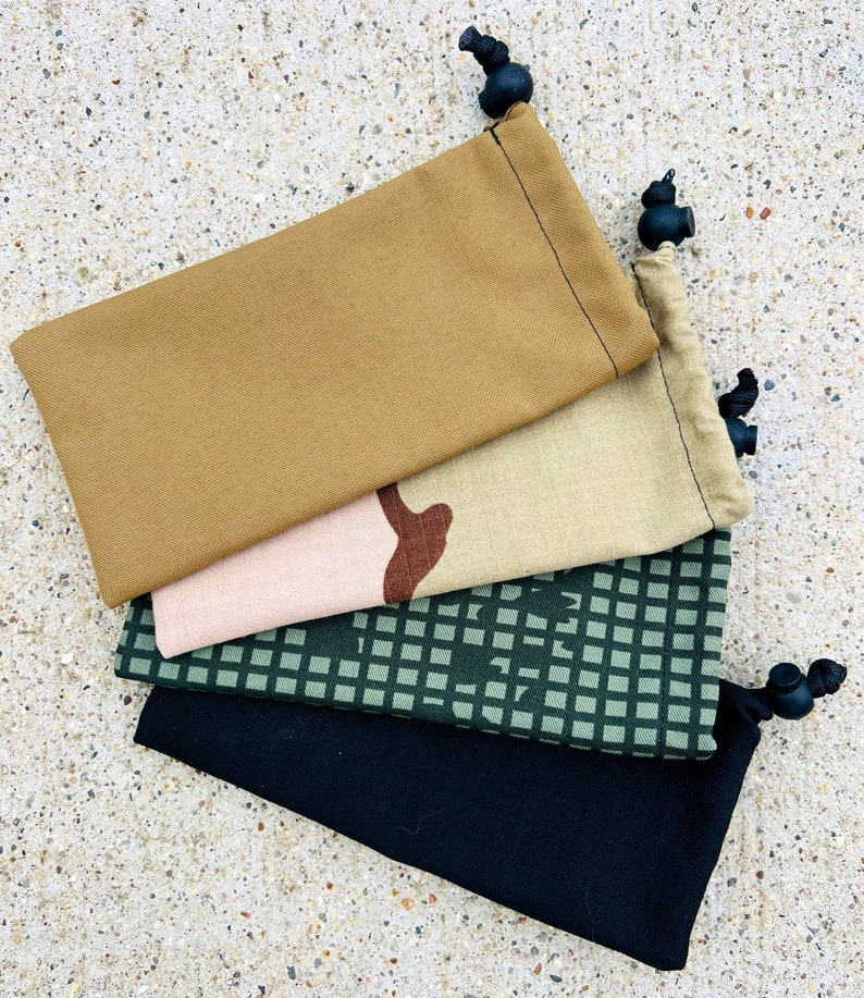 May include: Four drawstring bags made of different fabrics. The top bag is a solid brown colour, the second bag is a camouflage pattern, the third bag is a green and white chequered pattern, and the bottom bag is black.