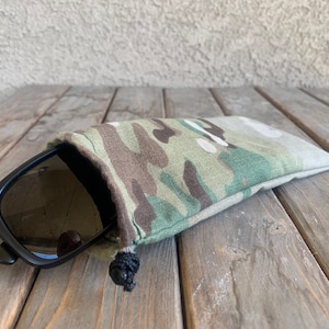 K&ouml;nnte beinhalten: Ein Camouflage-Beutel mit Kordelzug und einer schwarzen Sonnenbrille darin.