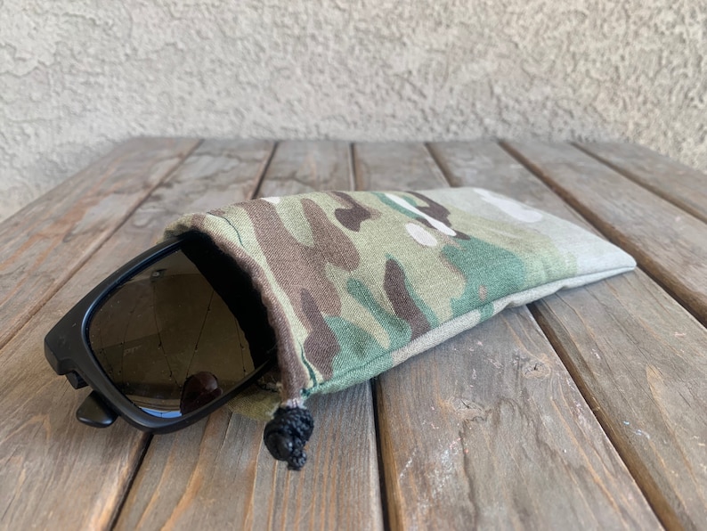 K&ouml;nnte beinhalten: Ein Camouflage-Beutel mit Kordelzug und einer schwarzen Sonnenbrille darin.
