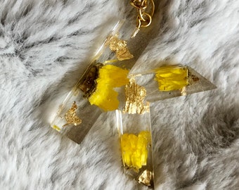 May include: A gold key chain with a clear resin charm shaped like a letter T. The charm is filled with yellow glitter and gold flakes.