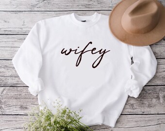 May include: White sweatshirt with the word "wifey" written in black cursive script.