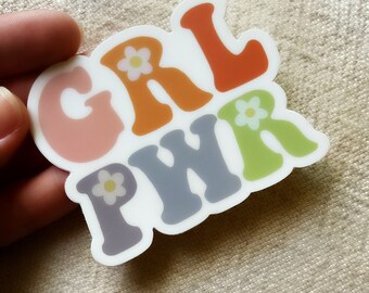 May include: A sticker with the words "GRL PWR" in colourful, stylized letters. Each letter has a white flower with a yellow centre.