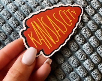 May include: A red arrowhead-shaped sticker with the text "KANSAS CITY" in yellow lettering.