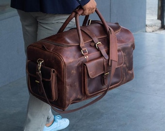 May include: A brown leather duffel bag with a long strap and multiple pockets. The bag has a distressed look and is made of high-quality leather.