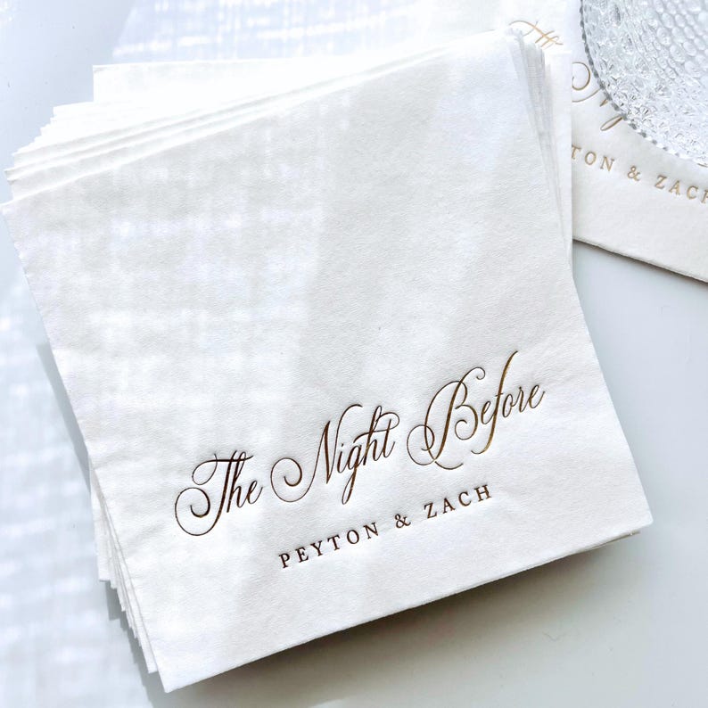 May include: A stack of white napkins with gold foil lettering that reads "The Night Before Peyton & Zach".