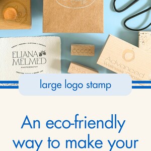 May include: A collection of wooden stamps with various designs, including a logo for "Vibe Dance Company", a logo for "Eliana Melmed Photography", and a logo for "Lavena Creative". The stamps are arranged on a light blue surface with a brown paper bag and a white canvas bag in the background. The text "large logo stamp" is visible in the image. The text "An eco-friendly way to make your brand stand out!" is also visible in the image.  The image also shows a variety of ink pads in different colors, including black, blue, green, and red.
